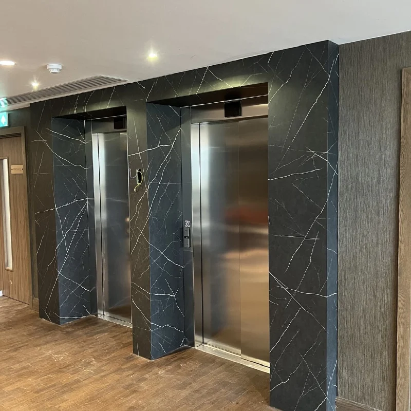 Chrome elevator doors with a black marble vinyl wrap on the surrounding walls.