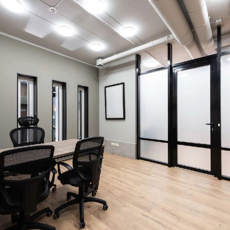 Industrial-style meeting room with a table, chairs, and frosted glass walls.