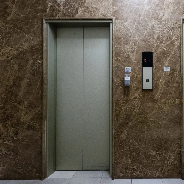 Light-gray elevator doors surrounded by a brown marble vinyl wrap.