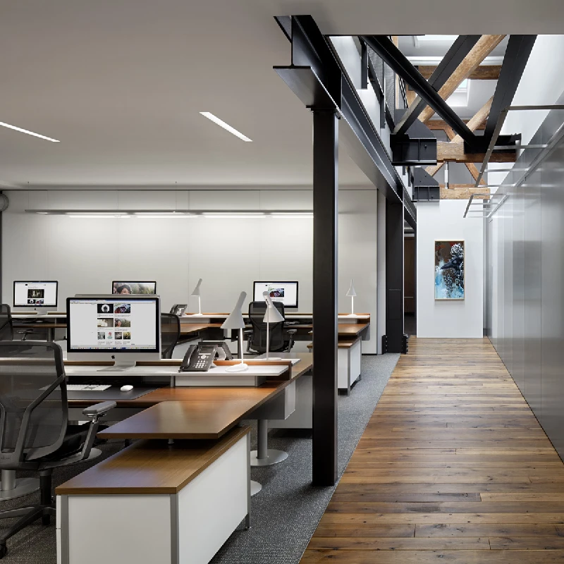 Modern office with open-plan desks, computers, and visible structural beams.