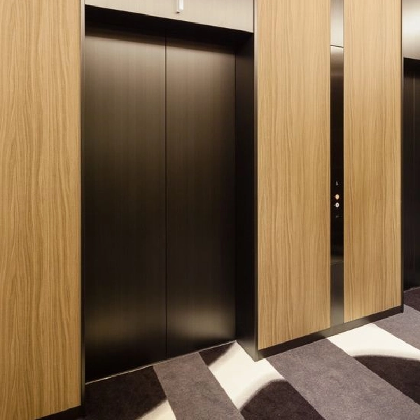 Vinyl-wrapped elevator doors with a woodgrain finish on the surrounding walls.
