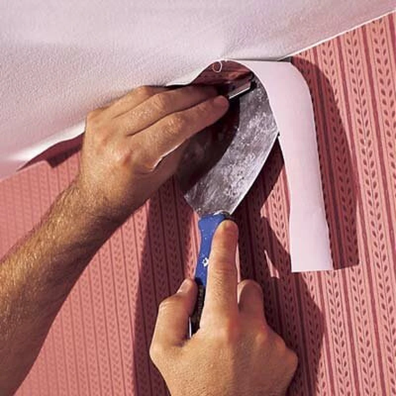 person using a putty knife to smooth and fix wallpaper in a corner.